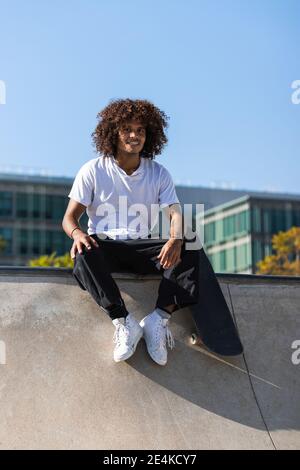 Mann ruht sich aus, während er mit Skateboard auf der Sportrampe sitzt Skateboard Park Stockfoto