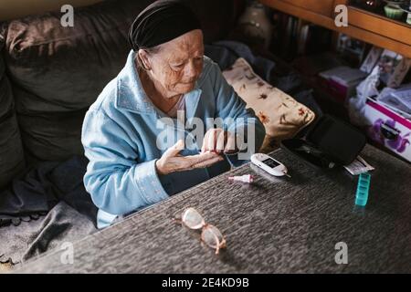 Ältere Frau, die im Wohnzimmer auf Diabetes getestet wird Zu Hause Stockfoto