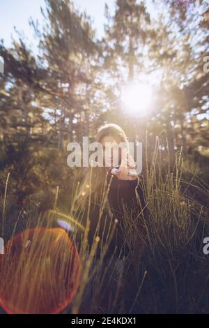 Junge Frau gestikuliert, während sie inmitten von Pflanzen im Wald steht Sonniger Tag Stockfoto