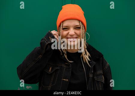 Glückliche Hipster Frau mit geflochtenen Haaren gegen grüne Wand Stockfoto