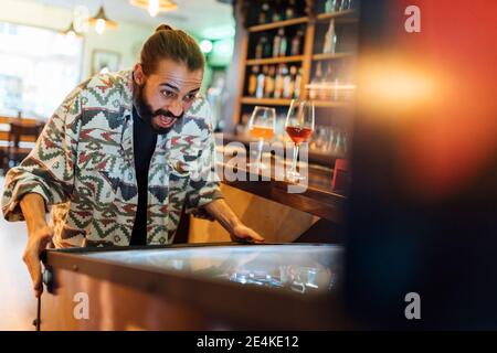 Fröhlicher bärtiger Mann spielt Flipper in der Bar Stockfoto