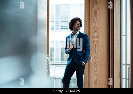 Nachdenklich junge gut aussehende Geschäftsmann hält Smartphone, während weg zu schauen Gegen das Fenster im Büro Stockfoto