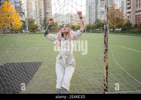 Modische junge Frau mit geschlossenen Augen lehnt auf Goalpost Netz Im Fußballfeld Stockfoto