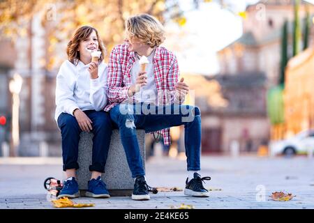 Lächelnder Junge und Mann, der Eis isst, während er darauf sitzt Bank Stockfoto