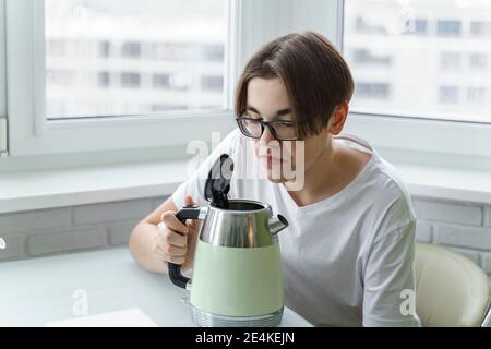 Ein junger Mann in Brille und weißem T-Shirt riecht Unangenehm vom Wasserkocher Stockfoto