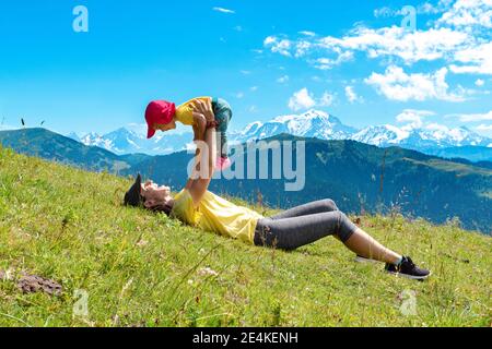 Mutter, die auf Gras im Col des Aravis, Haute-Savoie, Frankreich liegt, das Mädchen abholt Stockfoto