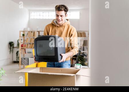 Junger Mann beim Bewegen Fernseher in Pappkarton packen In ein neues Zuhause Stockfoto
