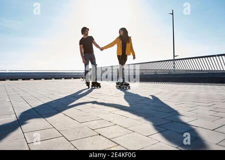 Junges Paar, das sich beim Rollschuhlaufen anschaut pier an sonnigen Tagen Stockfoto
