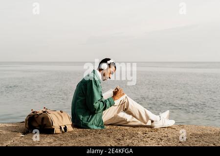 Junger Mann mit Kopfhörern, der auf dem Seeweg Tagebuch schreibt Stockfoto