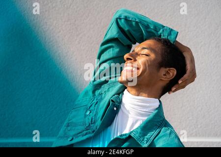 Mann lächelt, während stehen mit geschlossenen Augen gegen bunt Wand Stockfoto