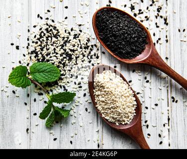 Gesundes Essen und Trinken Konzept. Schwarze und weiße Sesamsamen in einem Löffel auf einem Holztisch Stockfoto