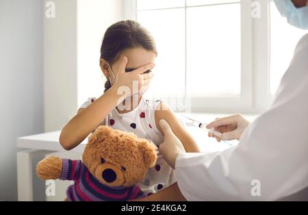 Kleines Mädchen Angst vor Spritze Nadel deckt Gesicht beim bekommen Grippeschutzimpfung in der Klinik Stockfoto