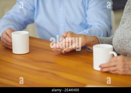 Ein verliebter älterer Partner hält sich die Hände, während er am Tisch sitzt Und eine Tasse Tee genießen Stockfoto