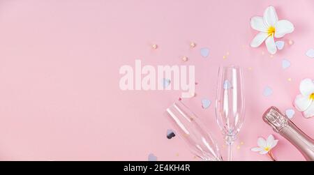 Zwei leere Sektgläser und eine Flasche Champagner mit weißen Frangipani-Blumen und kleiner Herzdeko auf rosa Hintergrund, Kopierraum Stockfoto