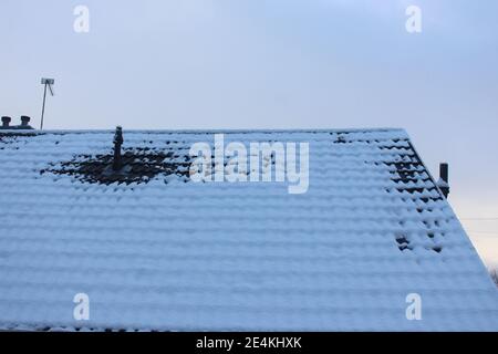 Ein Foto von einem Dach mit Antenne und Kaminen, bedeckt von einer dünnen Schicht von Neuschnee. Stockfoto