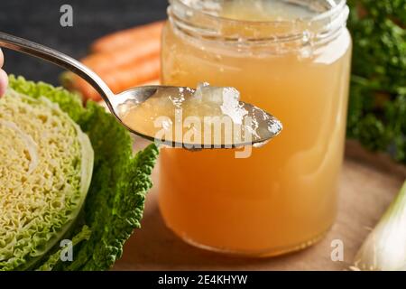 Abgekühlte Rinderbrühe auf einem Löffel, mit frischem Gemüse im Hintergrund Stockfoto