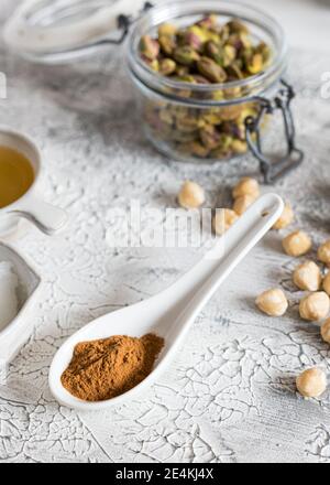 Nahaufnahme eines weißen Keramiklöffels voller Zimt neben einigen Haselnüssen auf einem rustikalen grauen Hintergrund. Stockfoto