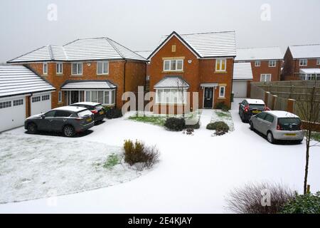 Unberührter Neuschnee bedeckt Straßen, Wege, Autos und Gras auf einer modernen Wohnsiedlung in Lancashire, Großbritannien Stockfoto