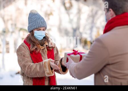 Nicht erkennbarer Mann, der der Frau in der Gesichtsmaske ein Geschenk gibt Stockfoto