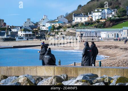 Lyme Regis, Dorset, Großbritannien. Januar 2021. UK Wetter: Ein heller, sonniger und kalter Tag im Badeort Lyme Regis. Während der dritten nationalen Sperre genießen die Einheimischen am fast menschenleeren Strand eine Flasche Kaffee. Kredit: Celia McMahon/Alamy Live Nachrichten. Stockfoto