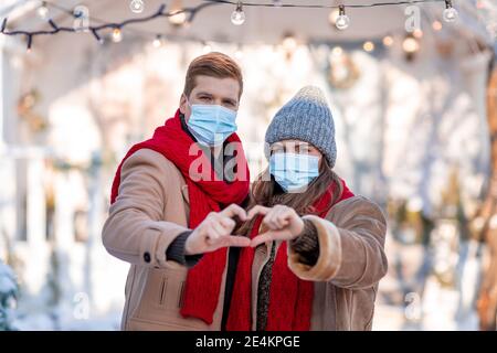 Paar in Gesichtsmasken mit Herz-Symbol, zu Fuß durch die Straße Stockfoto