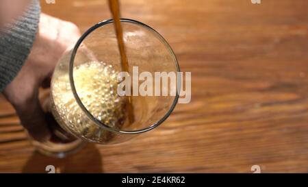 Von oben gießt dunkles Bier aus einer Dose in eine Glas auf einem Holztisch Stockfoto