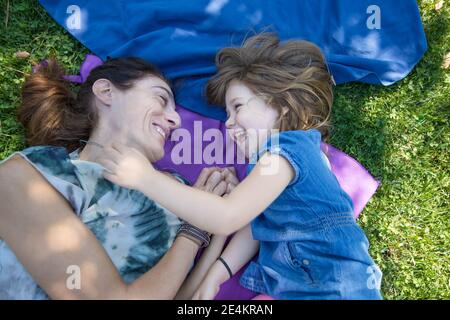 Vier Jahre alte blonde Kind und Frau Mutter lachen zusammen Liegen auf Handtüchern im grünen Gras des Parks Stockfoto