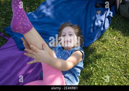 Vier Jahre alte blonde Mädchen liegen auf Handtücher in der Grünes Gras des Parks mit Hand in Bein suchen und Lächelnd Stockfoto