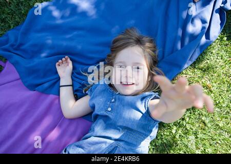 Vier Jahre alte blonde Mädchen liegen auf Handtücher in der Grünes Gras des Parks mit der Hand nach oben zu versuchen Berühren Sie Kamera Stockfoto