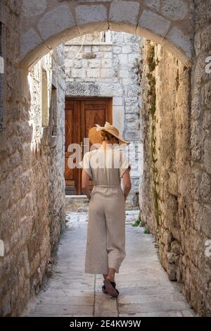 Rückansicht der schönen blonden jungen weiblichen Reisenden tragen Stroh Sonnenhut Sightseeing und genießen Sommerurlaub in einer alten traditionellen Küstenstadt Stockfoto