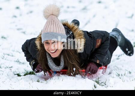 Chippenham, Wiltshire, Großbritannien. Januar 2021. Als Chippenham Bewohner zu ihrem ersten Schnee des Jahres aufwachen, wird eine Frau in einem lokalen Park in Chippenham abgebildet, während sie auf einem Schlitten einen Hügel hinuntergleitet. Quelle: Lynchpics/Alamy Live News Stockfoto