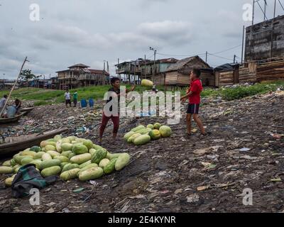 Iquitos, Peru - Sep 2019: Männer verlagern Früchte aus einem Boot. Am Ufer des Flusses Itaya ist im Hintergrund eine enorme Verschmutzung zu sehen. Niedriger A Stockfoto