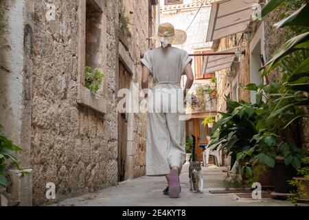 Rückansicht der schönen blonden jungen weiblichen Reisenden tragen Stroh Sonnenhut Sightseeing und genießen Sommerurlaub in einer alten traditionellen Küstenstadt Stockfoto