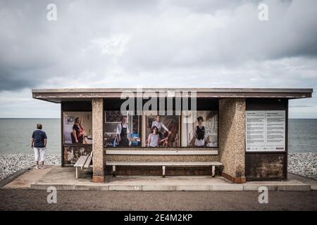 Betonschutz am Meer mit einmundem Mann, der hinausschaut Zum Meer allein verlassenen Strand Bilder von Menschen grauen Sturm Wolken über Bushaltestellen Stockfoto