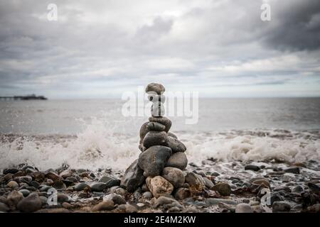 Haufen von Steinen gestapelt balancierende Küste Meer Lappen Oben Kieselsteine Turm grau dramatische Sturmwolken sammeln sich über Wellen Krachende Harmonie Zen Meer Stockfoto