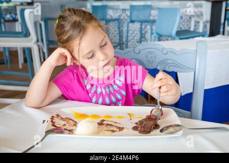 Süße vier Jahre alte blonde Mädchen, Linkshänder, Essen mit Löffel süße Dessert: Schwarze Schokolade, Vanille-Eis, Erdbeeren und Mangosauce, Sitti Stockfoto