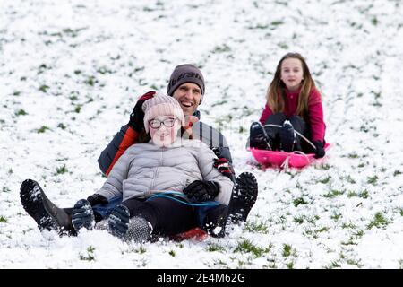 Chippenham, Wiltshire, Großbritannien. Januar 2021. Während die Chippenham-Bewohner zu ihrem ersten Schnee des Jahres aufwachen, werden ein Paar und ein Kind in einem lokalen Park in Chippenham abgebildet, während sie auf Schlitten einen Hügel hinuntergleiten. Quelle: Lynchpics/Alamy Live News Stockfoto