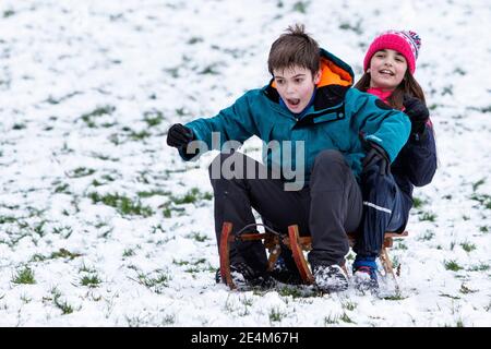 Chippenham, Wiltshire, Großbritannien. Januar 2021. Als Chippenham-Bewohner zu ihrem ersten Schnee des Jahres aufwachen, werden zwei Kinder in einem lokalen Park in Chippenham fotografiert, während sie auf einem Schlitten einen Hügel hinuntergleiten. Quelle: Lynchpics/Alamy Live News Stockfoto