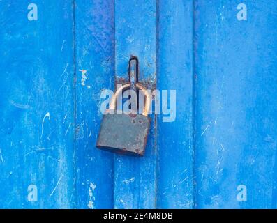 Industrielle vintage verschlossene Eingangstür mit blätternder blauer Farbe. Tür aus rostig gepunktetem Metall mit Vorhängeschloss im Retro-Stil. Stockfoto