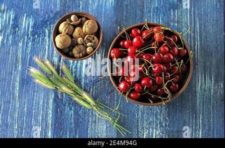 Frische rote Kirschen und Walnüsse in einer Schüssel auf einem Blauer Holztisch Stockfoto