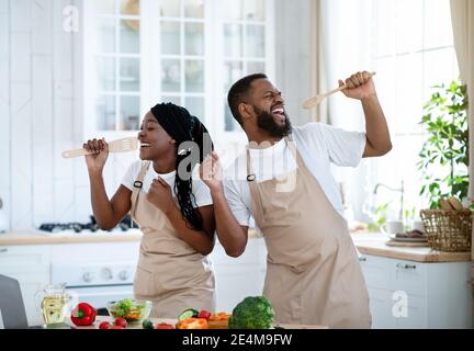 Küchenkonzert. Fröhliche Schwarze Paar Spaß Beim Kochen Zusammen Zu Hause Stockfoto