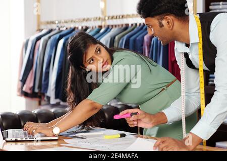 Schöne junge weibliche indische Schneider arbeiten auf Laptop, wenn sie Kollege Zeichnung Mode Skizze Stockfoto