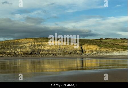 Dunraven Bay mit nassem Sand und Reflexen der nahe gelegenen Klippe, Glamorgan Heritage Coast, South Wales. Stockfoto