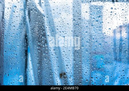 Regentropfen auf dem Glas bei Regenwetter.die glitzernde, glänzende Wasseroberfläche auf dem Glas.Wassertropfen in Form von Kugeln oder Kugeln.Blaue Regentropfen bac Stockfoto