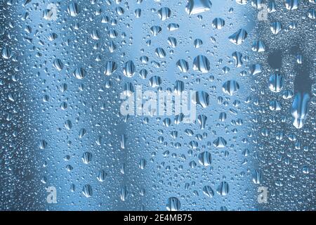 Regentropfen auf dem Glas bei Regenwetter.die glitzernde, glänzende Wasseroberfläche auf dem Glas.Wassertropfen in Form von Kugeln oder Kugeln.Blaue Regentropfen bac Stockfoto