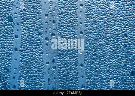 Regentropfen auf dem Glas bei Regenwetter.die glitzernde, glänzende Wasseroberfläche auf dem Glas.Wassertropfen in Form von Kugeln oder Kugeln.Blaue Regentropfen bac Stockfoto