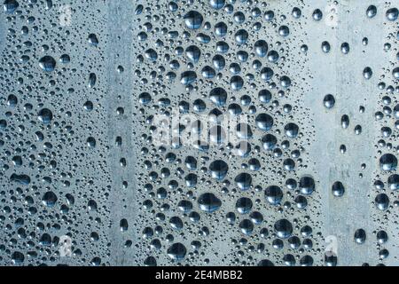 Regentropfen auf dem Glas bei Regenwetter.die glitzernde, glänzende Wasseroberfläche auf dem Glas.Wassertropfen in Form von Kugeln oder Kugeln.Blaue Regentropfen bac Stockfoto