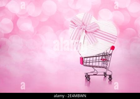 Warenkorb mit großem Geschenk mit Herzform auf Rosa mit Bokeh Hintergründe.Liebe einkaufen Stockfoto