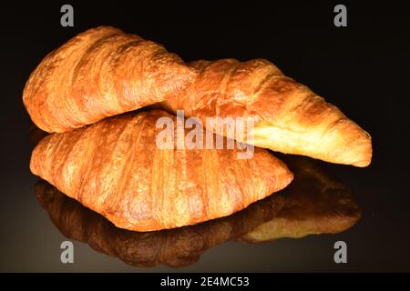 Drei ganze duftende, frische, knackige Croissants auf schwarzem Hintergrund, Nahaufnahme. Stockfoto