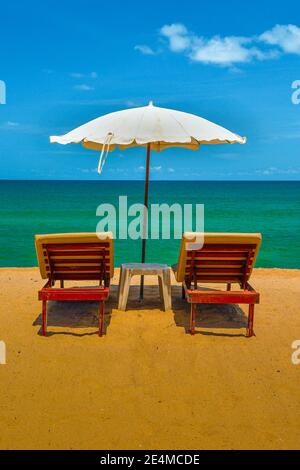 Rückansicht eines Paar Holzliegen und weißen Sonnenschirm auf einem tropischen Strand, mit goldenem Sand und blauem Himmel und Meer. Stockfoto